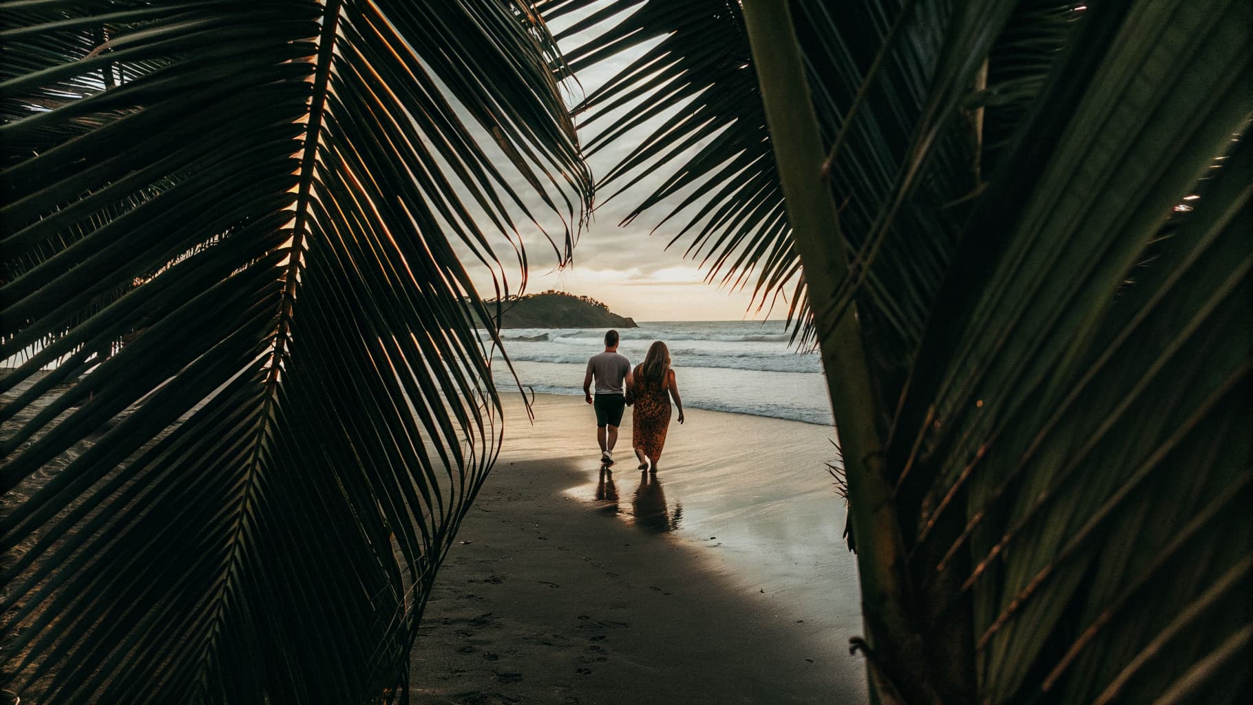 Couple walking hand in hand along a golden sand beach in Jaco, Costa Rica at sunset