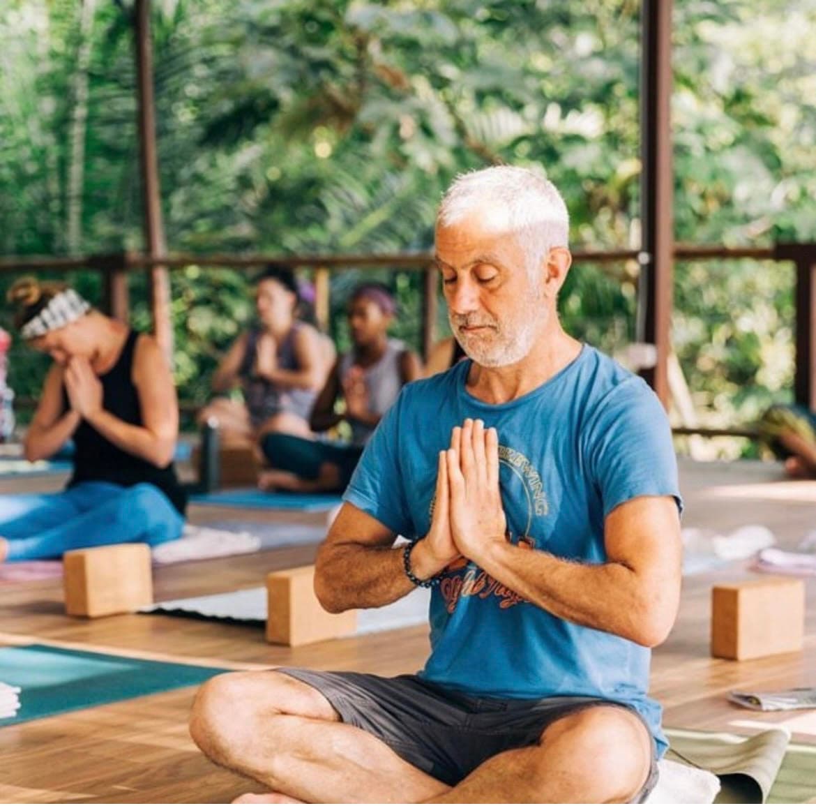 Senior yoga instructor leading group meditation session at jungle retreat in Costa Rica